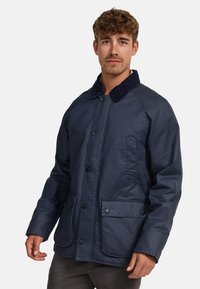 Veste bleu marine avec un col en velours côtelé, deux poches avant et une fermeture à boutons. Tissu texturé avec une coupe décontractée et des manches longues.