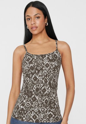 Femme aux longs cheveux noirs portant des boucles d'oreilles argentées en forme de créoles et un haut sans manches gris foncé à motifs avec de fines bretelles.