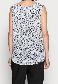 Top senza maniche a fiori con fiori bianchi e azzurri su uno sfondo nero, indossato con pantaloni neri larghi, vista da dietro.