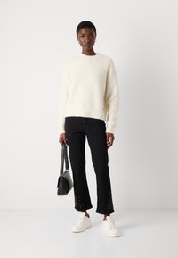 Crème trui met een zachte textuur, zwarte jeans met geborduurde zoom, witte sneakers en een zwarte handtas. Eenvoudig, modern ontwerp.
