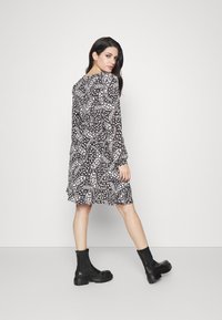 Vestido preto e branco com padrão, mangas longas, corte solto e bainha com babados. Combinado com botas pretas de tornozelo robustas.