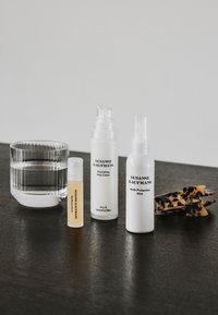 Verre d'eau claire, trois produits de soin Susanne Kaufmann et une pince à cheveux écaille sur une surface sombre contre un fond uni.