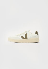 Beige sneakers with a textured fabric upper, olive green side accents, and a chunky beige sole. Model name "V-90" on the heel.