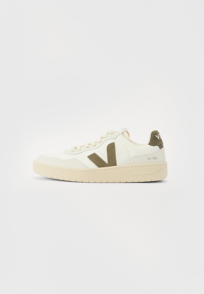 Beige sneakers with a textured fabric upper, olive green side accents, and a chunky beige sole. Model name "V-90" on the heel.