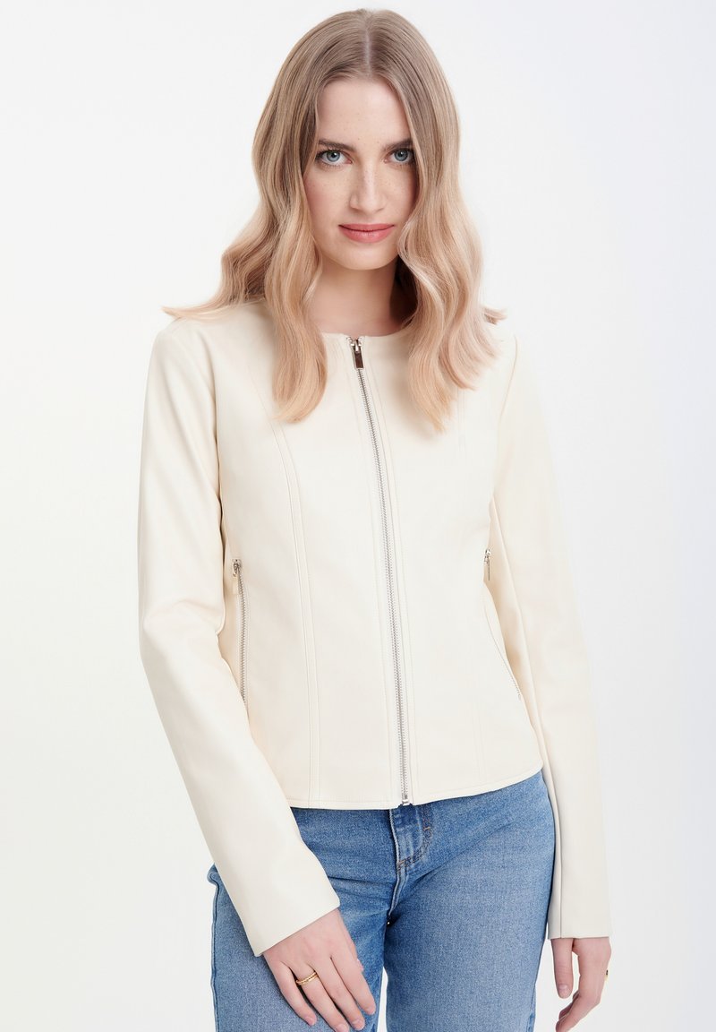 Giacca in ecopelle color crema con zip frontale, tasche laterali e silhouette aderente. Maniche lunghe con una texture liscia.
