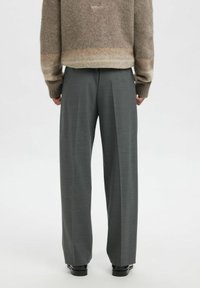 Grå bukser med vide ben og frontfolder. Materialet ser glatt ut. Kombinert med en beige, strukturert genser. Enkle svarte sko er synlige.