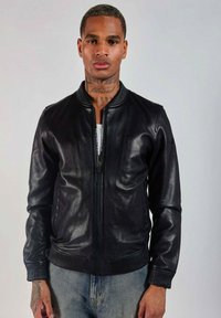 Veste bomber en cuir noir avec une fermeture éclair à l'avant, un col et des poignets côtelés, offrant une texture lisse et une coupe ajustée.