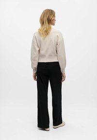 Felpa corta beige chiaro con spalle scese, abbinata a pantaloni neri a righe e calzature beige. Design in tessuto semplice e testurizzato.