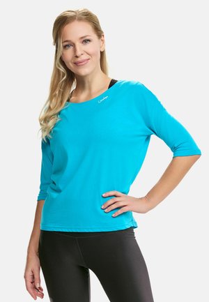 Turquoise long-sleeve top with a round neckline and three-quarter sleeves. Soft fabric, featuring subtle logo accent on the chest.