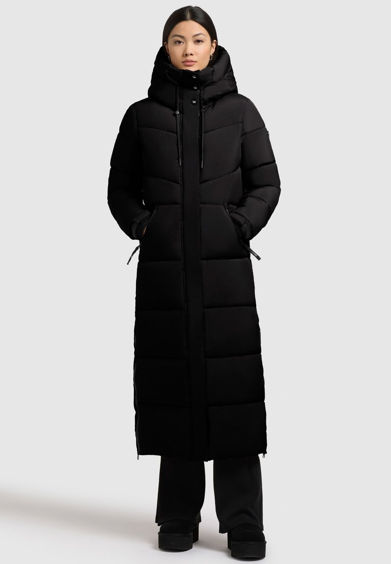 Ilgas juodas pūstas paltas su aukštu kaklu, užtrauktuku ir reguliuojamomis raištelėmis; turi siuvinėtas dalis ir šonines kišenes.