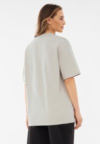 Világosszürke pamut póló rövid ujjakkal, laza szabással és kerek nyakkivágással. Oldalsó hasítékokkal és sima textúrával rendelkezik.