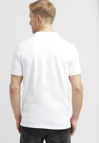 Polo shirt bianco in cotone con maniche corte, design semplice e colletto classico. Tessuto liscio senza motivi o accenti visibili.