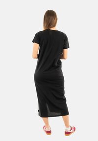 Robe noire mi-longue à manches courtes, avec une coupe décontractée et une fente latérale ; associée à des chaussures de sport rouges et blanches.