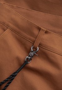 Bruine stof met een gladde textuur, voorzien van een metalen sluiting en een zwarte trekkoord. Zichtbare stiksels langs de randen.