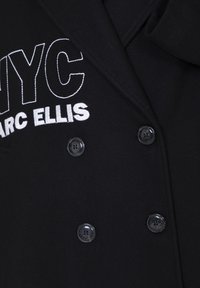 Giacca nera doppiopetto realizzata in tessuto testurizzato con ricamo bianco della scritta "NYC" e "MARC ELLIS"; presenta bottoni neri.