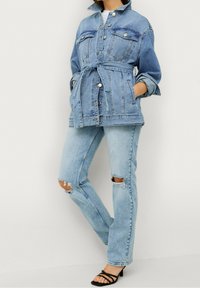 Ljust blå denimjacka med framfickor och bälte i midjan, tillsammans med ljusblå slitna jeans och svarta klackskor med remmar.