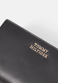 Black leather wallet with a smooth texture featuring a gold embossed "TOMMY HILFIGER" logo at the corner. Neat stitching visible.