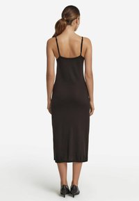 Svart midi-klänning med tunna band, figursydd form och sidoklyftor. Slät, mjuk textur. Bärs med svarta klackskor.