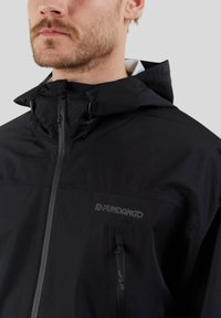 Zwarte windbreaker jacket met een ritssluiting aan de voorkant, verstelbare capuchon en een borstzak. Voorzien van textuurstof en een logo aan de zijkant.