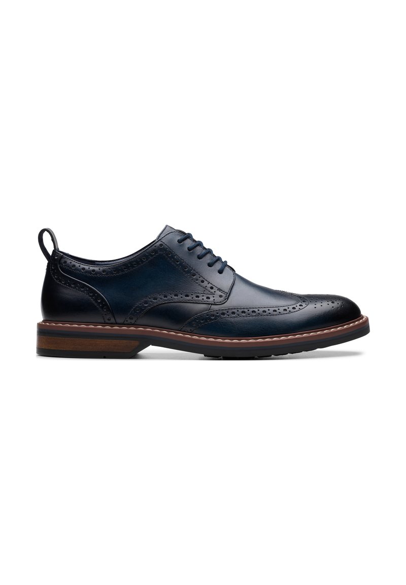 Navy leather dress shoe with brogue detailing, a rounded toe, and a contrasting light brown sole. Features laces and a pull tab.