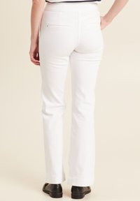 Pantaloni bianchi a gamba dritta con una texture liscia, tasche posteriori e una vita di media altezza, abbinati a scarpe nere basse.