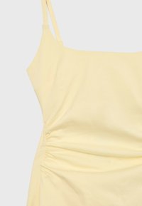 Robe jaune sans manches avec fines bretelles et détail de tissu froncé sur le côté gauche sur fond uni.