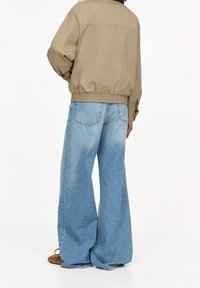 Beige bomber jacket with elastic hem and cuffs paired with loose, light blue wide-leg jeans featuring faded wash and back pockets.