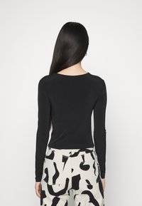 Svart långärmad topp med rund halsringning, kombinerad med beige byxor med ett abstrakt svart mönster. Söt och slät tygtextur.