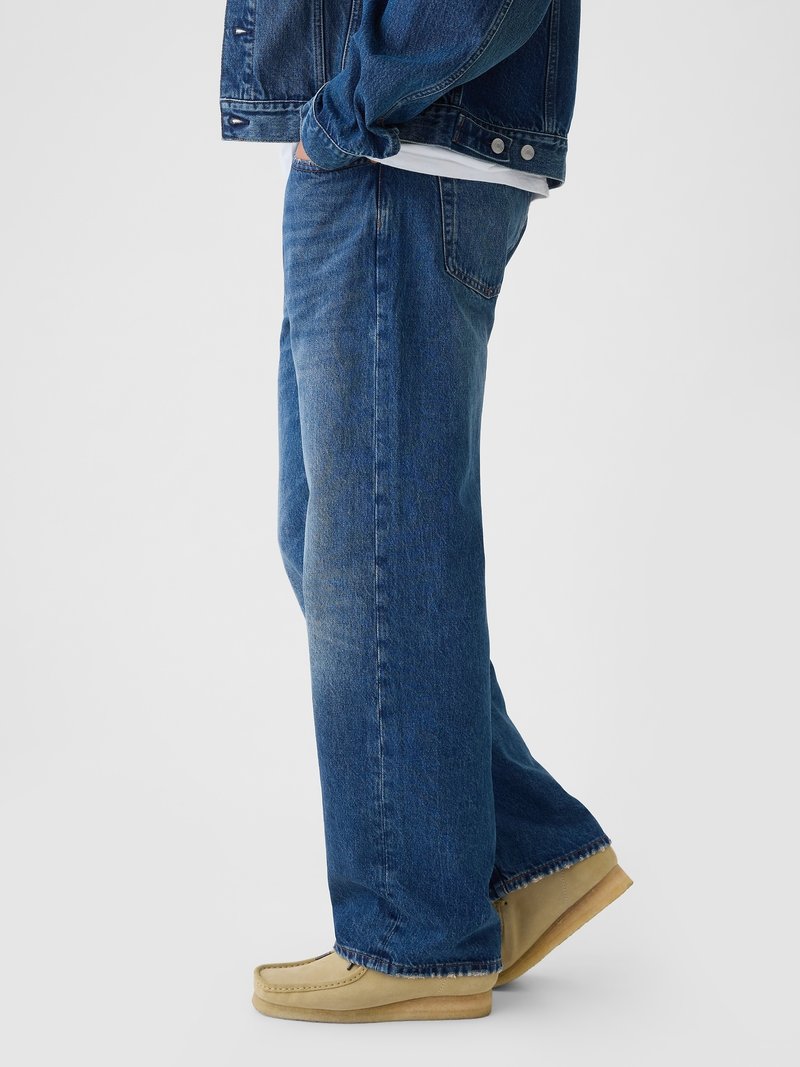 Blaue Denim-Jeans mit lockerer Passform, die eine ausgeblichene Waschung, gerades Bein Design und Nähdetails aufweisen, kombiniert mit beigen Mokassin-Schuhen.