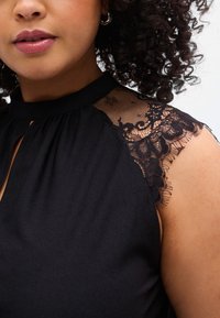 Μαύρο αμάνικο ρούχο με υψηλό λαιμόκοψη, με απαλές δαντελένιες λεπτ ομέρειες στους ώμους. Απαλή υφή, εφαρμοστή γραμμή.