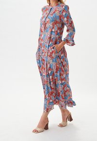 Robe longue multicolore avec un motif floral en rouge, bleu et rose. Confectionnée dans un tissu léger, avec des manches longues et des poches latérales.