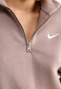 Brun zip-up sweatshirt i mjukt tyg, med hög krage, silverdragkedja och vit Nike-logotyp på vänster bröst.