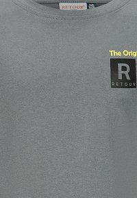 Tessuto grigio con un piccolo logo giallo e nero che recita "The Original R RETOUR" vicino al colletto, etichetta della taglia 140 9/10 visibile.