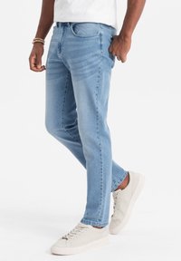 Vaaleansiniset denim-farkut, joissa on slim fit -muotoilu, hienovarainen kuluminen ja viisi taskua. Tyylitelty kerma-ainesneakersien ja valkoisen t-paidan kanssa.