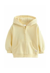 Haut à zip couleur jaune clair fabriqué en tissu doux. Il est doté d'une capuche, de deux poches avant et de bords côtes aux manches et à l'ourlet.