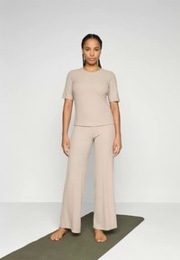 Outfit composto da un top a coste beige e pantaloni a gamba larga, con scollo a giro e maniche corte, indossato da un modello a piedi nudi.