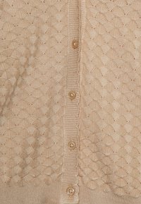 Cardigan de punto beige con un patrón de diamante texturizado, bordes acanalados y seis botones redondos y brillantes en la parte delantera.