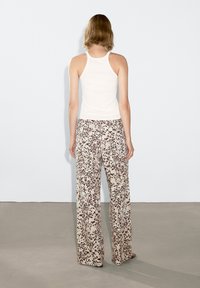 Witte, strakke tanktop gecombineerd met beige, brede broek met een donkerbruin gespikkeld patroon. Glad materiaal met een vloeiende pasvorm.