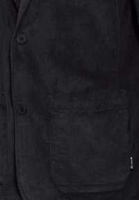 Svart kordjacka med en texturerad yta, knäppning framtill och en ficka på framsidan, med en etikett på sidan.