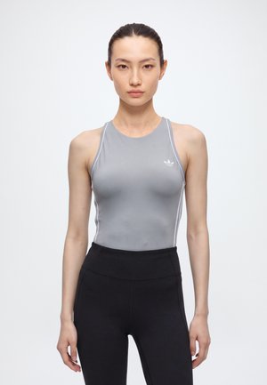 Жена представя сив потник Adidas и черен клин на изчистен бял фон.