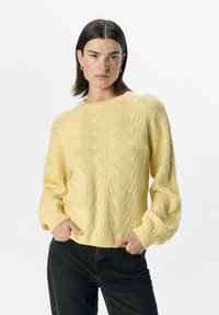 Yellow knitted sweater with a textured pattern, round neckline, and ribbed cuffs. Paired with dark jeans, showcased against a plain background.