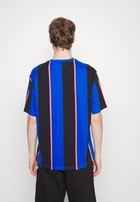Tricou scurt cu mânecă, în dungi albastre și negre, cu linii verticale și accente colorate. Fabricat dintr-un material moale, având o tăietură lejeră.