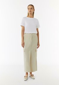 White short-sleeve t-shirt paired with a high-waisted beige midi skirt featuring side pockets. The model wears light beige shoes.