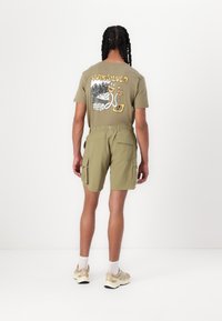 Olijfgroene katoenen T-shirt met een grafisch ontwerp op de achterkant, gecombineerd met bijpassende cargoshorts. Heeft zakken en een elastische tailleband.