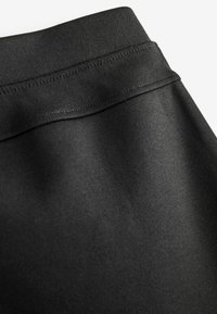 Zwarte stoffen leggings met een gladde textuur, een brede tailleband en platlock naden voor duurzaamheid. De stof lijkt rekbaar en aansluitend.