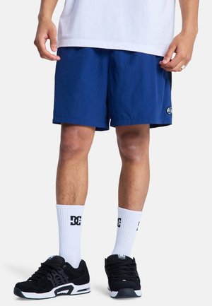 Granatowe sportowe szorty o gładkiej fakturze z małą naszywką z logo, w połączeniu z czarnymi tenisówkami i białymi skarpetami za kostkę z logo.