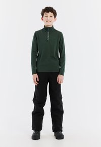 Pullover verde con maniche lunghe e colletto a mezza zip; pantaloni neri e stivali impermeabili. Design semplice, texture liscia e senza motivi visibili.