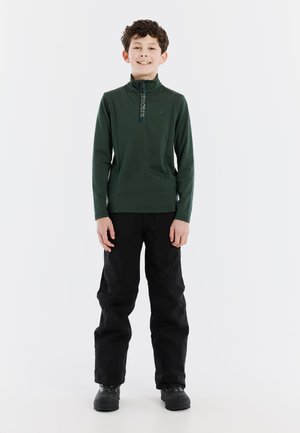 Pullover verde con maniche lunghe e colletto a mezza zip; pantaloni neri e stivali impermeabili. Design semplice, texture liscia e senza motivi visibili.