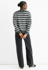 Striped sweater in dark gray with light gray stripes, knit material, rounded neckline, and ribbed cuffs. Paired with black wide-leg pants.