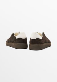 Sneakers in suede marrone con un accento in pelle bianca sul tallone. Presentano una suola in gomma testurizzata e un design semplice e a profilo basso.